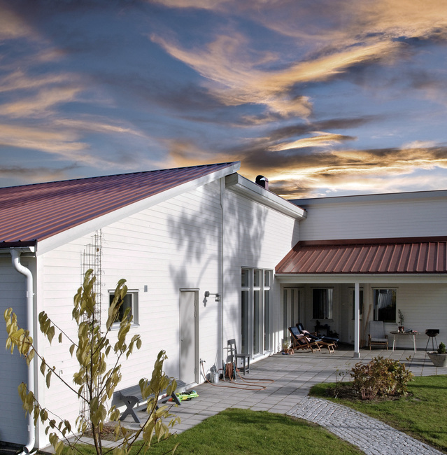 A white house with red Plannja Panneplate roofing and white gutters
